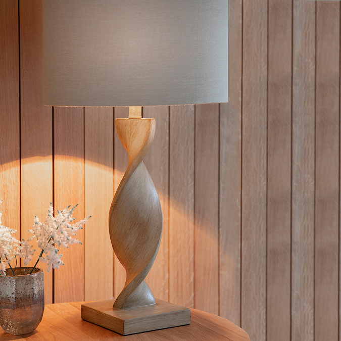 close up on lamp with wooden twisted base and linen shade, on an entryway table emitting a warm glow