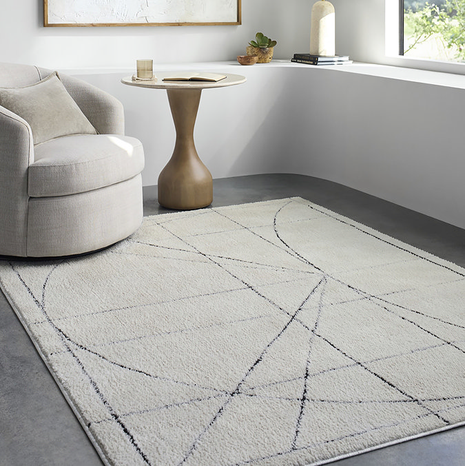 image of ivory rug with black blueprint-inspired lines on it, on grey floor of modern apartment living room
