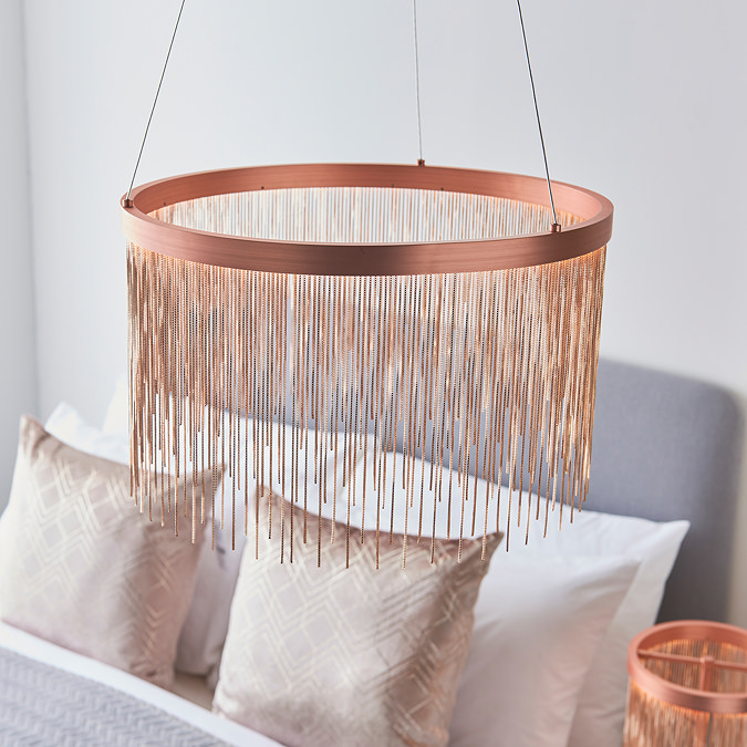image of brushed copper tasselled light hanging from ceiling above grey bed with light gold cushions on it