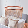 image of brushed copper tasselled light hanging from ceiling above grey bed with light gold cushions on it