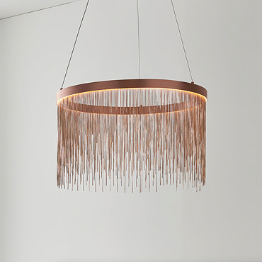 image of brushed copper tasselled light hanging from ceiling above grey bed with light gold cushions on it