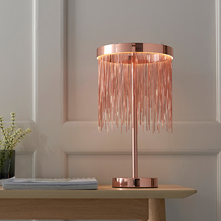 image of brushed copper fringed table lamp on a light oak console table in front of a cream panelled wall