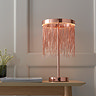 image of brushed copper fringed table lamp on a light oak console table in front of a cream panelled wall
