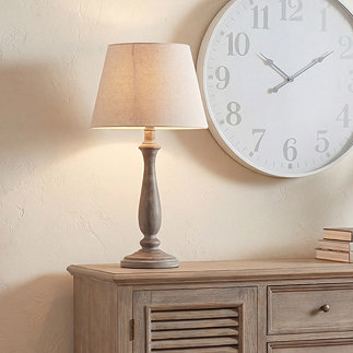 image of light brown sculpted lamp with linen shade on washed wood sideboard
