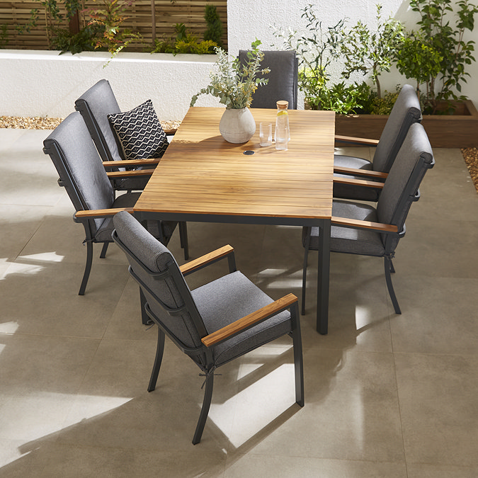 image taken from slightly above of wooden slatted tabletop of rectangular garden dining table with six grey chairs tucked around it, featuring matching teak arms