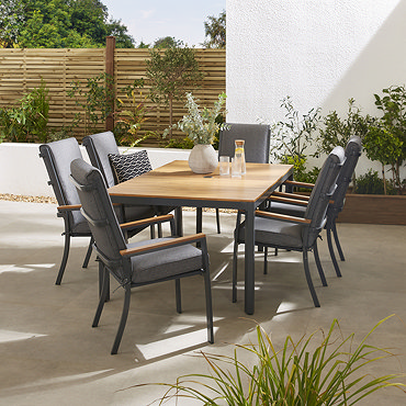 image taken from slightly above of wooden slatted tabletop of rectangular garden dining table with six grey chairs tucked around it, featuring matching teak arms