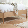 close up on bottom of an oak bed with sleek wooden legs and soft green throw over the edge of the duvet