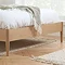 close up on bottom of an oak bed with sleek wooden legs and soft green throw over the edge of the duvet