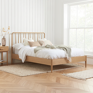 image of slatted oak bed with spindled headboard against a panelled cream wall, next to a warm wood bedside table with a fluffy rug underneath