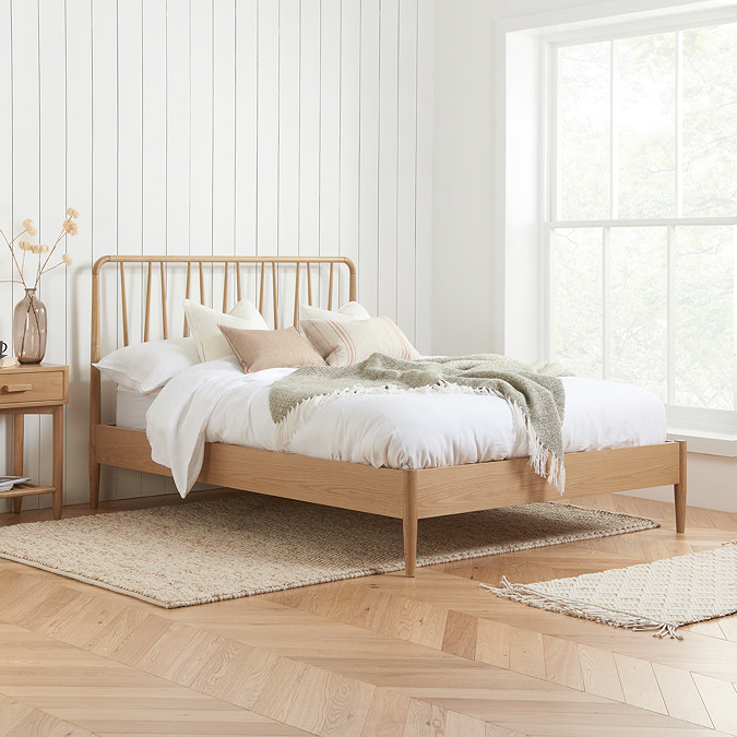 image of slatted oak bed with spindled headboard against a panelled cream wall, next to a warm wood bedside table with a fluffy rug underneath