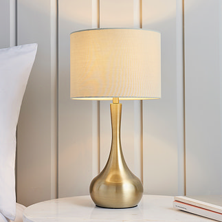 image of brass and taupe table lamp with rounded base on a bedroom side table in front of cream panelled wall