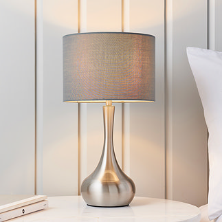 image of modern table lamp with nickel slim body with dark grey fabric shade, on a cream bedside table in front of a cream panelled wall