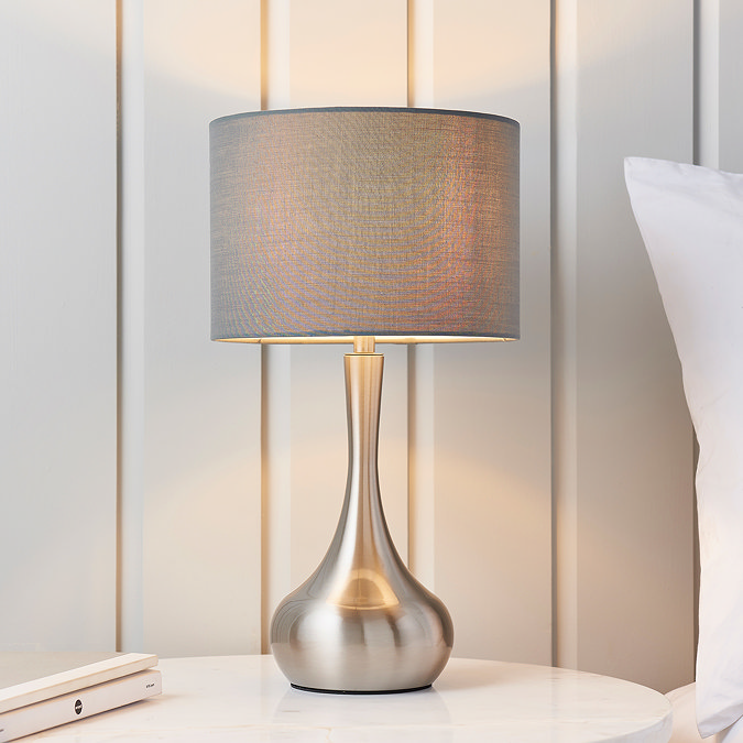 image of modern table lamp with nickel slim body with dark grey fabric shade, on a cream bedside table in front of a cream panelled wall