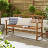 image of three seater bench in oil teak finish, with patterned cushions, in front of a white wall in a garden