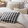 image of black and white checkered fringed cushion on bed with matching natural version