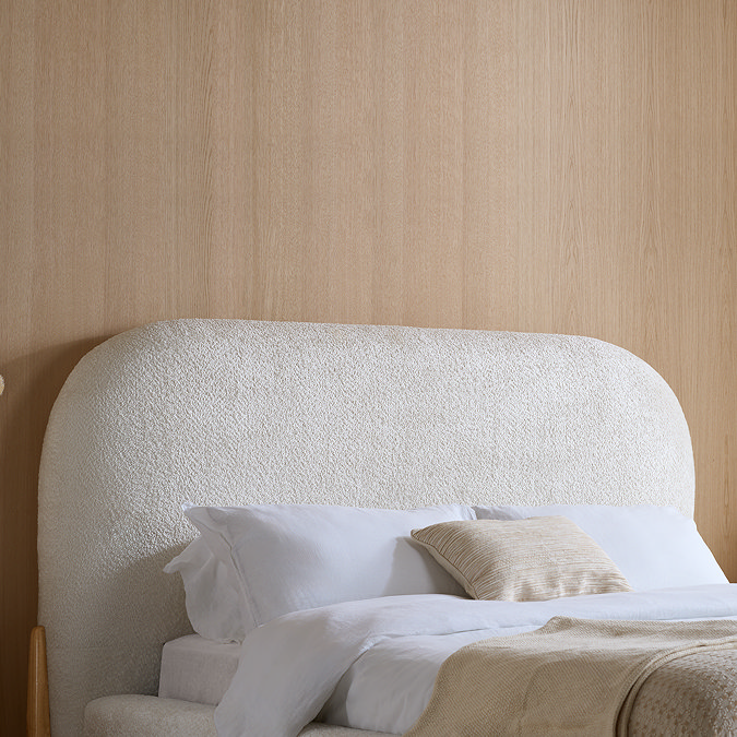 close up image of curved white boucle headboard against light brown wall