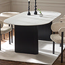 image of oval marble white dining table with black fluted pedestal legs on white rug with cream chenille dining chairs