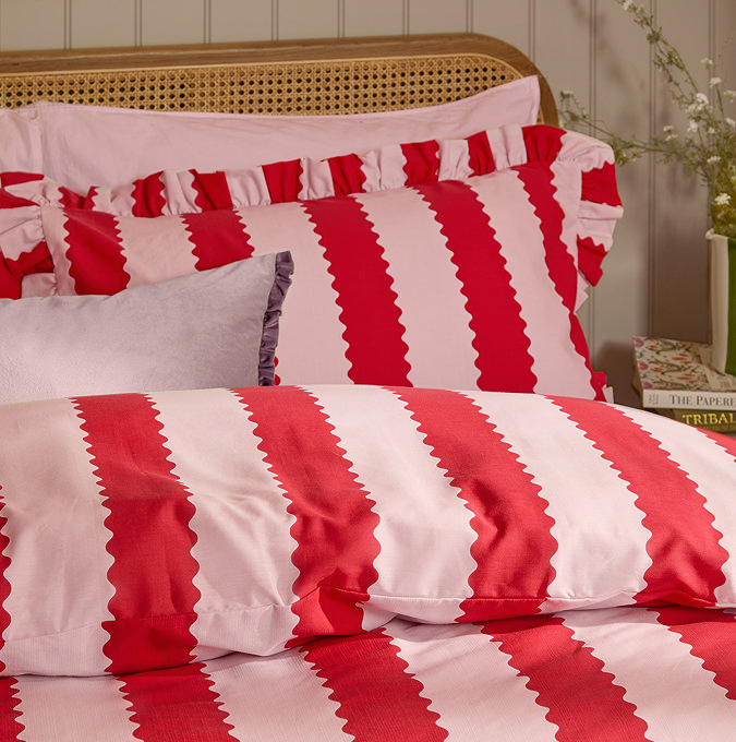 close up image of top of bed covered in red and pink striped duvet, with matching cushions edged in ruffle trim
