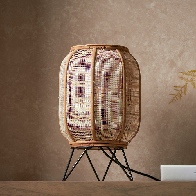image of natural rounded rectangular table lamp with black metal legs on a side table in front of a warm brown wall