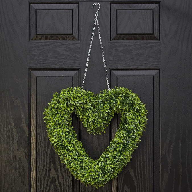 image of a heart-shaped green wreath hanging on a black front door by a chain