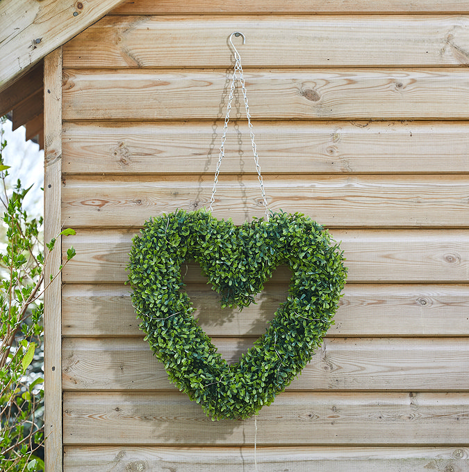 image of green heart-shaped wreath hanging on the side of a shed by a chain
