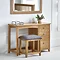 image of solid oak single dressing table with grey padded stool tucked underneath, pushed up against light grey wall with wooden mirror hanging above