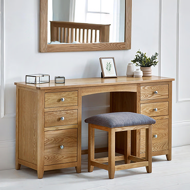 image cut out on white background of solid wood dressing table with six drawers and padded stool pushed underneath
