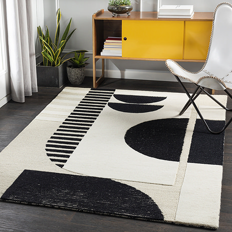image of cream and black geometric rug on grey wood flooring of home office, in front of bright yellow modern cupboard and potted plant