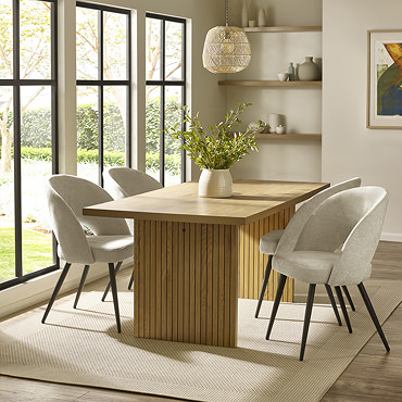 image of rectangular oak dining table with fluted rectangular pillar legs, no chairs around it, on a cream rug in front of long dining room windows