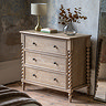 image of limed oak three drawer chest with hand-crafted bobbin detail, against a distressed grey wall and topped with a lamp and faux plant