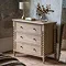 image of limed oak three drawer chest with hand-crafted bobbin detail, against a distressed grey wall and topped with a lamp and faux plant