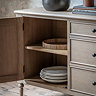 close up on limed oak sideboard with left door open to reveal two shelved filled with crockery