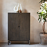 image of dark wood cabinet in front of a beige wall, topped with decorative accessories, next to a tall plant with light shining onto it