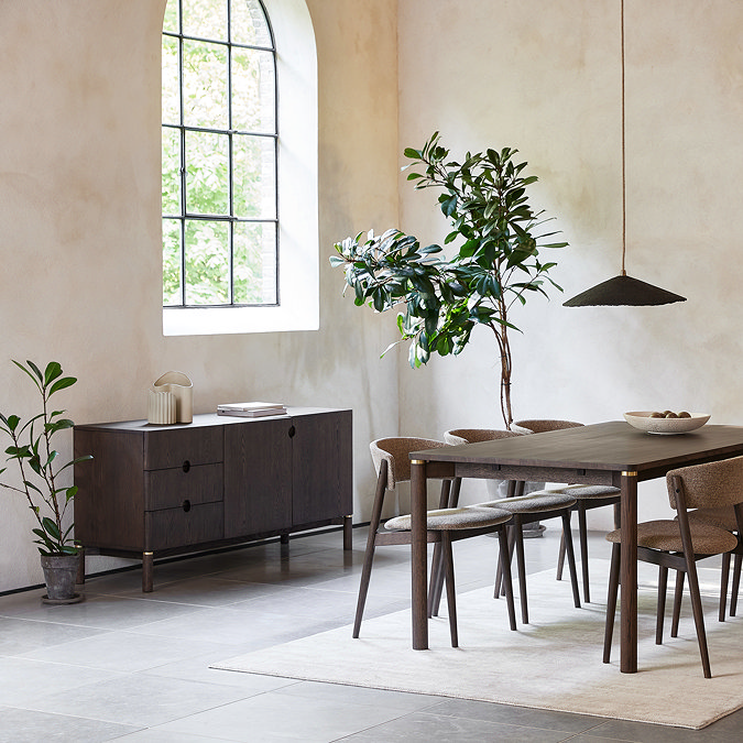 wide image of dining room with dark oak sideboard on the left side of the room, below an arched window with light streaming through