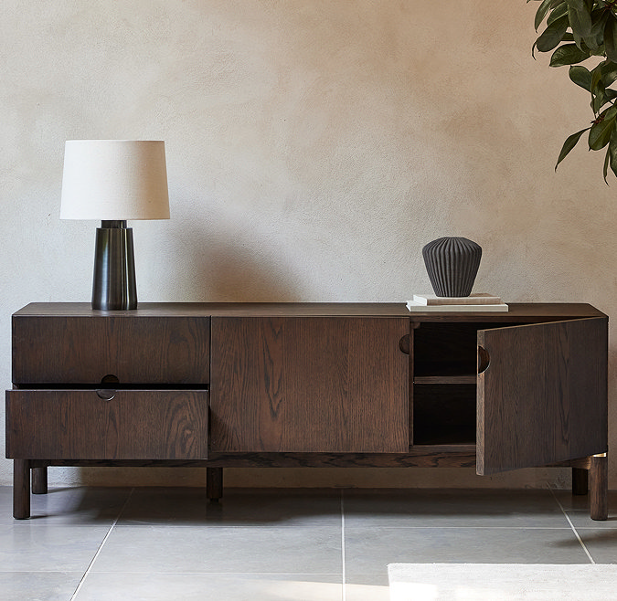 image of dark oak tv low-board with left bottom drawer open and right side door open, against a cream wall and on grey slate flooring