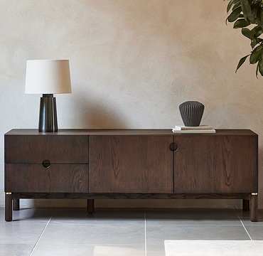 image of dark oak tv low-board with left bottom drawer open and right side door open, against a cream wall and on grey slate flooring