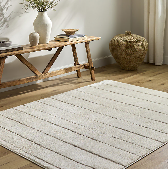 image of ivory striped soft rug on light wood flooring next to low bench