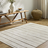 image of ivory striped soft rug on light wood flooring next to low bench
