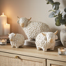 trio of ceramic highland cows in three sizes on a warm wood sideboard, surrounded by cosy candles.