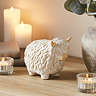 small ceramic highland cow displayed on a sideboard, surrounded by cosy candles and a potted plant.