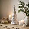 large ceramic christmas tree in a matte finish with a star on top, displayed on a sideboard surrounded by candles, small presents and a potted plant.