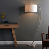 image of curved nickel floor light with natural linen shade, against a dark grey wall emitting warm light over an oak console table