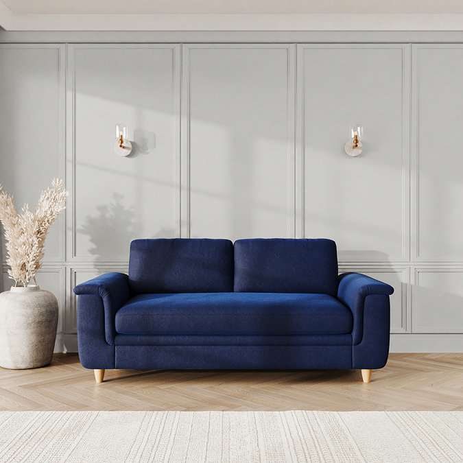 lifestyle image of large sofa with sculpted arms and light oak feet, in indigo velvet