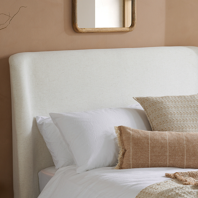 close up on linen headboard of cream ottoman bed, decked with pillows and clay coloured cushions