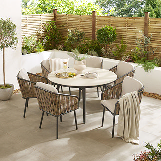image of round sintered stone table with black metal legs, and surrounded by six wicker dining chairs with black metal legs