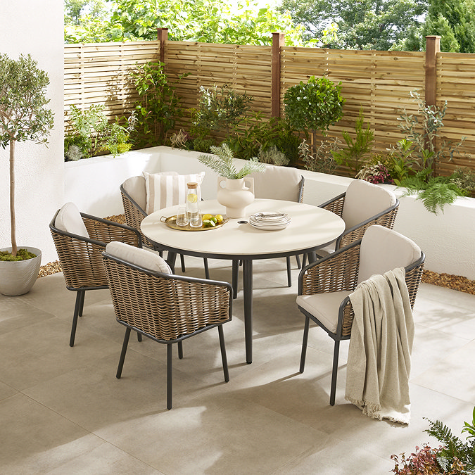 image of round sintered stone table with black metal legs, and surrounded by six wicker dining chairs with black metal legs