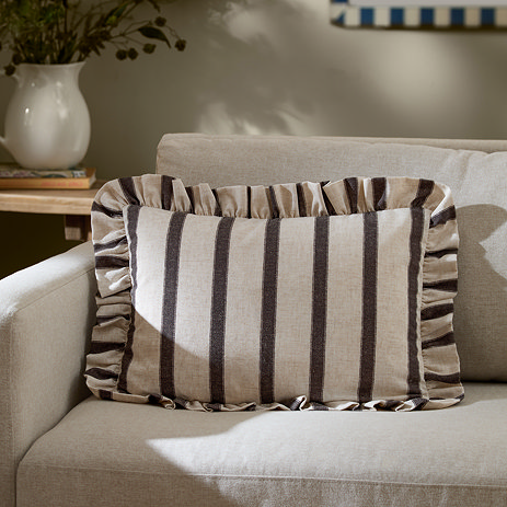 chocolate brown striped rectangle cushion placed on a cream sofa.