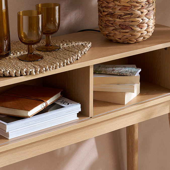 close up on oak console table with doors open, showing two shelves inside containing books and magazines