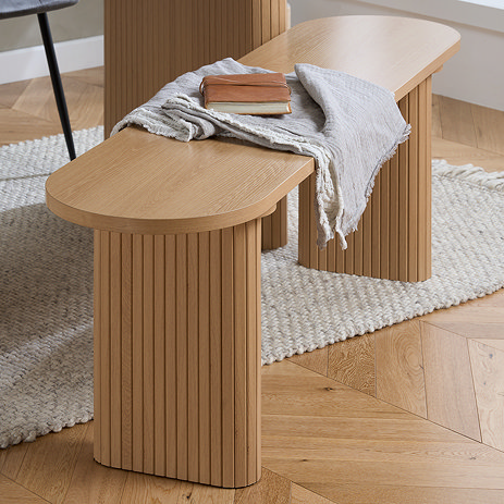 image of oval dining bench with oak effect and fluted style legs, on wooden flooring of dining room
