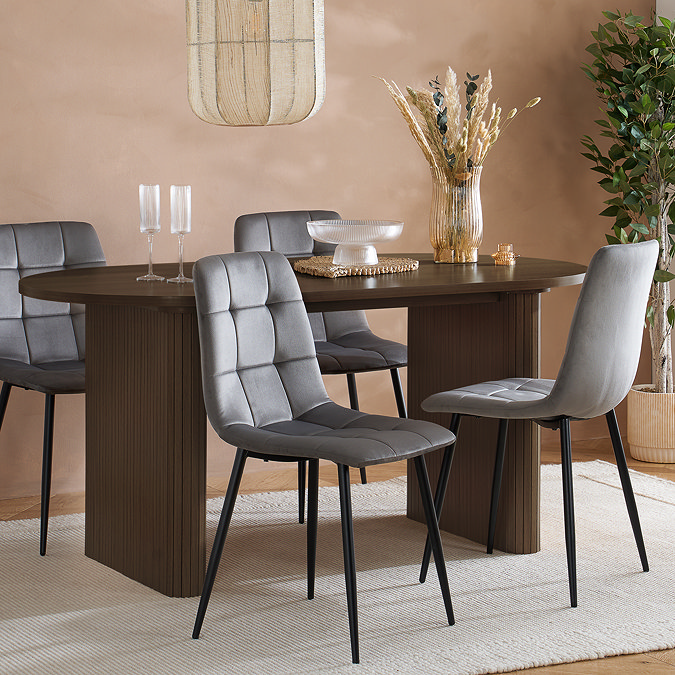 image of oval walnut dining table with fluted base, with four grey chenille dining chairs tucked into it on top of a rug